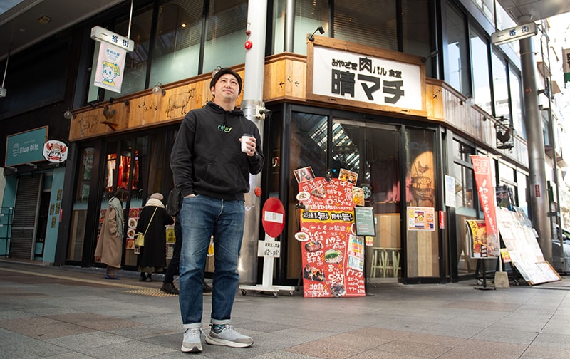relayの最初の掲載案件になった飲食店の前に立つ齋藤さん=宮崎市