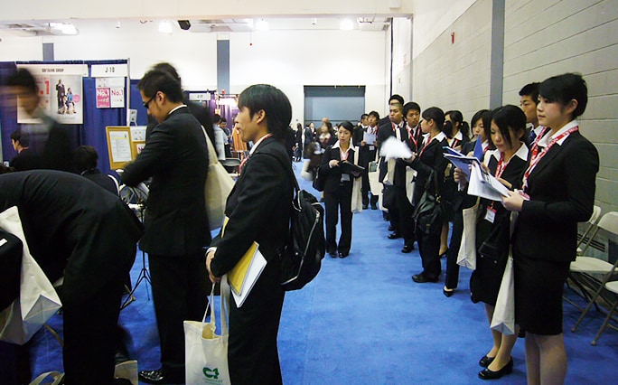 イベント会場でスーツを着た若い男女が並んで順番を待っている風景